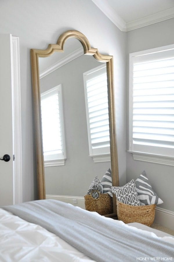 neutral master bedroom, full size leaning mirror w/wicker basket holding gray and white pillows