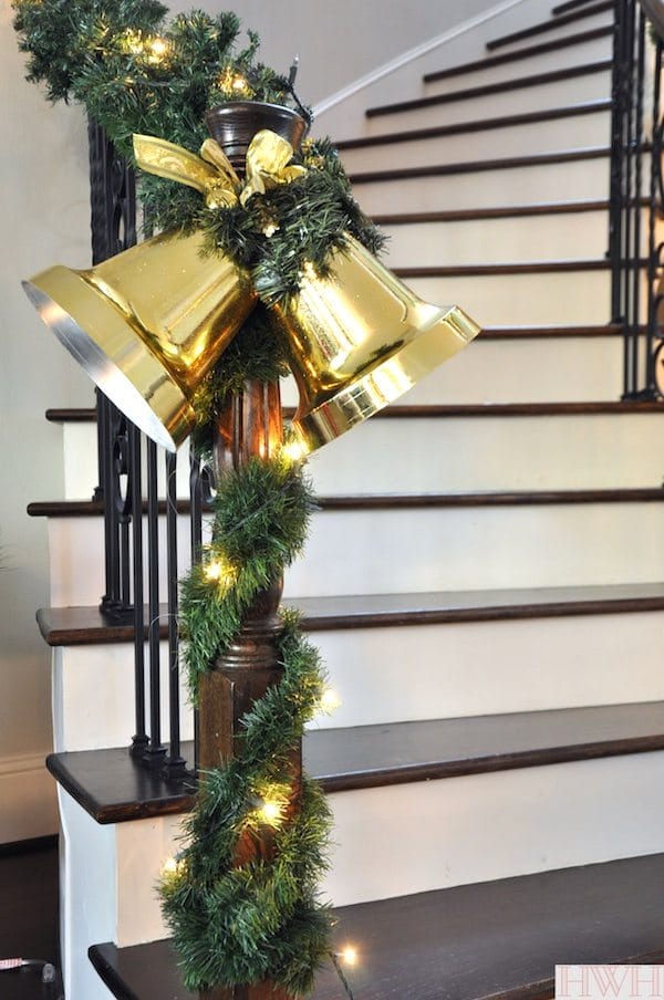 Festive holiday garland wrapped around the staircase with large gold bells - Merry Christmas! | Honey We're Home