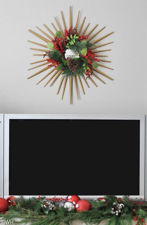 Festive holiday decor- berry and pinecone wreath hung from a gold starburst mirror| Honey We're Home